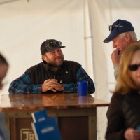 Man smiling at other man while he is sitting down with hands together